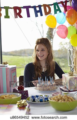 Stock Image - Teenage girl at table with birthday cake. Fotosearch