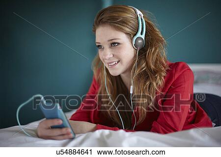 Stock Image - Teenage girl in bedroom listening to music. Fotosearch
