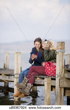 Teenage girls sitting on jetty listening to music View Large Photo Image Picture - Teenage girls sitting on jetty listening to music. Fotosearch