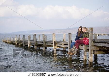 Teenage girls sitting on jetty View Large Photo Image Stock Photo - Teenage girls sitting on jetty. Fotosearch