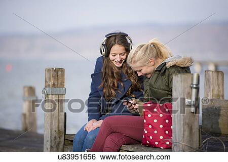 Teenage girls sitting on jetty listening to music View Large Photo Image Stock Photograph - Teenage girls sitting on jetty listening to music. Fotosearch