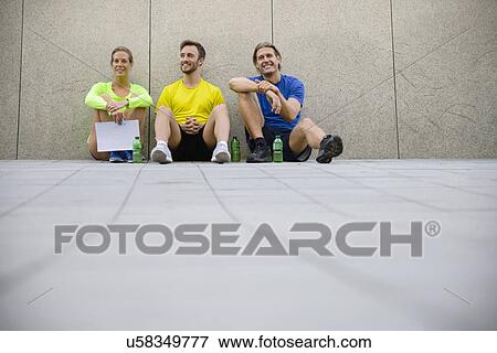 Stock Photo - Three friends sitting on floor wearing sports clothing. Fotosearch