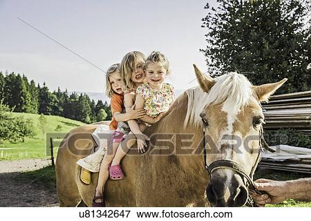 Stock Photo - Three young girls sitting on palomino horse. Fotosearch