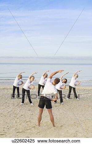 Stock Photography - Trainer and group of mature and senior women exercising on beach. Fotosearch
