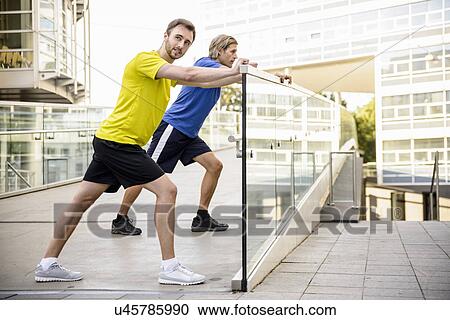 Stock Image - Two men leaning and stretching legs. Fotosearch