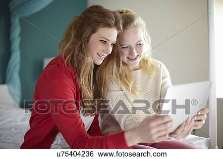 Two teenage girls looking at digital tablet in bedroom View Large Photo Image Stock Photograph - Two teenage girls looking at digital tablet in bedroom. Fotosearch