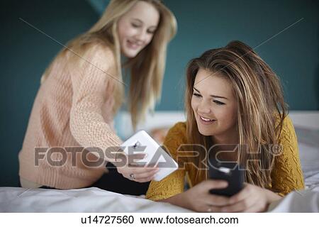 Two teenage girls looking at smartphones in bedroom View Large Photo Image Stock Image - Two teenage girls looking at smartphones in bedroom. Fotosearch