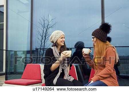 Two young adult women enjoying coffee on rooftop terrace View Large Photo Image Picture - Two young adult women enjoying coffee on rooftop terrace. Fotosearch