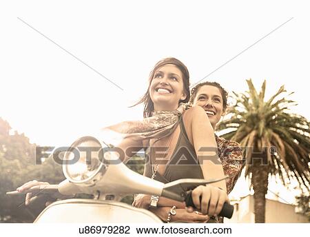 Two young female friends riding moped View Large Photo Image Stock Image - Two young female friends riding moped. Fotosearch
