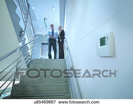 Stock Photo - View of thermostat in office stairwell with workers in meeting on stairs. Fotosearch