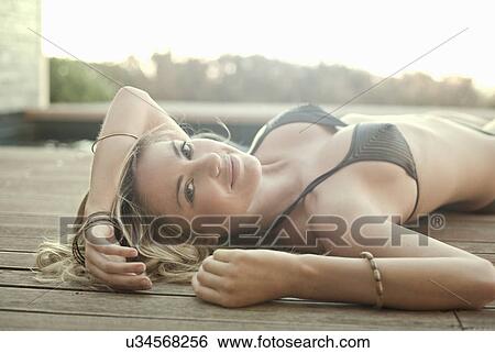 Stock Photograph - Woman in bikini lying on wooden decking. Fotosearch