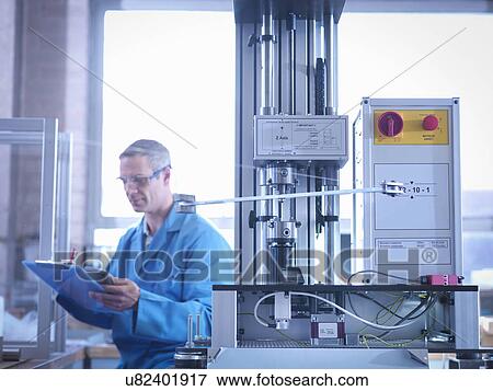 Stock Photo - Worker holding clipboard and using spring testing equipment for automotive use. Fotosearch