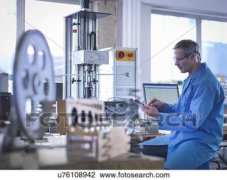 Stock Image - Worker in protective eyewear using spring testing equipment for automotive use. Fotosearch