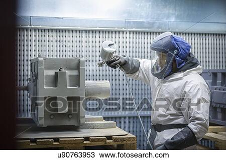 Stock Image - Worker paint spraying industrial gearboxes in factory. Fotosearch