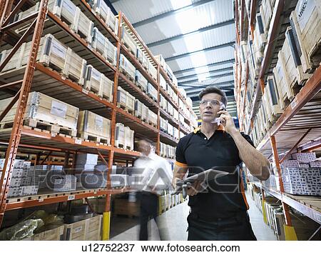 Worker using mobile phone and holding digital tablet in parts store in factory View Large Photo Image Stock Photo - Worker using mobile phone and holding digital tablet in parts store in factory. Fotosearch