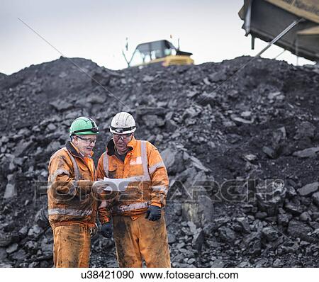 Stock Image - Workers in discussion in front of coal stocks in surface coal mine. Fotosearch