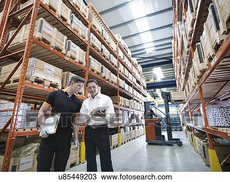Stock Image - Workers using digital tablet in parts store in factory. Fotosearch