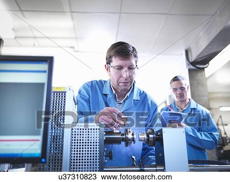 Stock Image - Workers using spring testing equipment for automotive use. Fotosearch