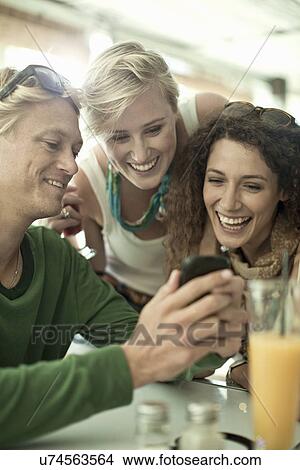 Young adult friends looking at cellphone in bar View Large Photo Image Picture - Young adult friends looking at cellphone in bar. Fotosearch