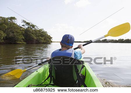 Stock Photography - Young boy paddling canoe on tranquil river. Fotosearch