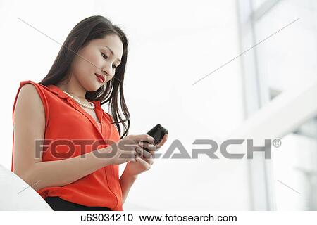 Stock Image - Young businesswoman reading texts on cellphone. Fotosearch