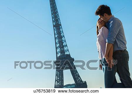 Stock Photo - Young couple embracing near Eiffel Tower, Paris, France. Fotosearch