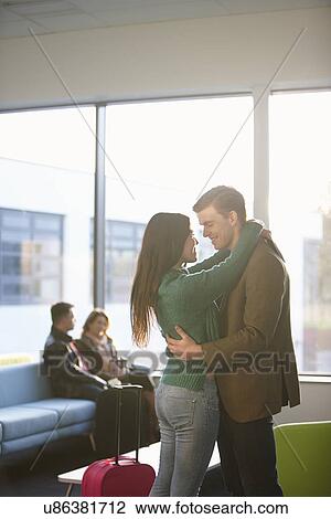 Stock Image - Young couple hugging in airport. Fotosearch