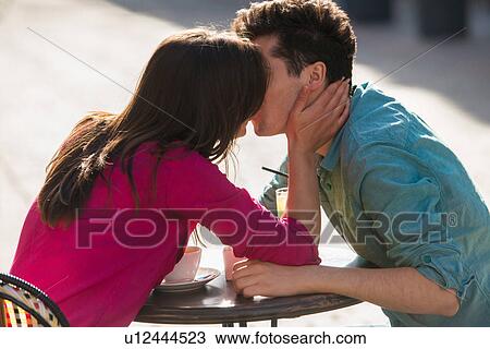 Stock Image - Young couple kissing at pavement cafe, Paris, France. Fotosearch