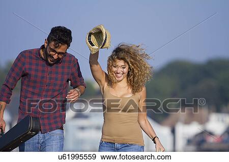 Stock Photo - Young couple laughing, woman holding hat. Fotosearch