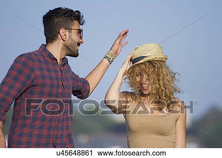 Stock Image - Young couple laughing, woman wearing hat. Fotosearch
