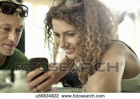 Young couple looking at cellphone in cafe bar View Large Photo Image Stock Image - Young couple looking at cellphone in cafe bar. Fotosearch