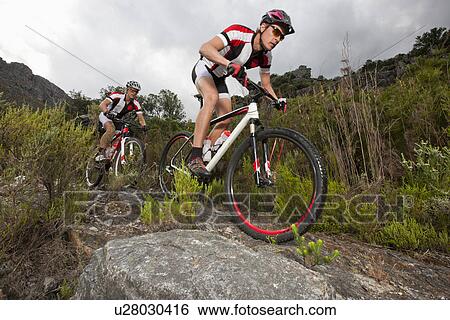 Stock Photograph - Young couple riding mountain bikes on dirt track. Fotosearch