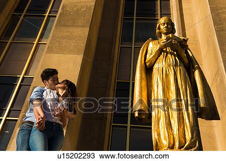 Stock Image - Young couple sharing a kiss next to statue, Paris, France. Fotosearch