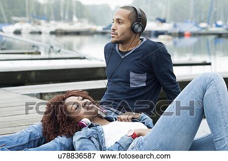 Stock Photo - Young couple sitting on jetty. Fotosearch
