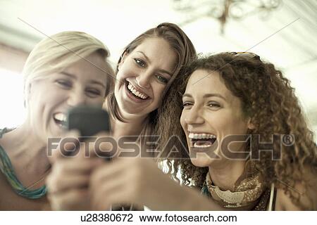 Young female friends looking at cellphone in cafe bar View Large Photo Image Stock Image - Young female friends looking at cellphone in cafe bar. Fotosearch