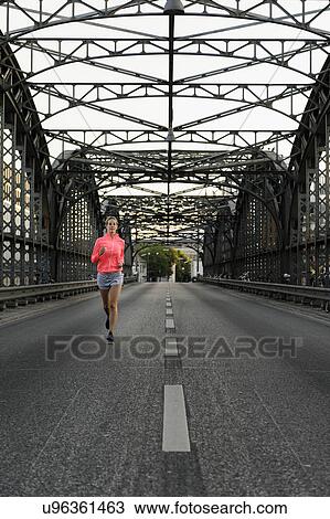 Stock Image - Young female runner across bridge. Fotosearch