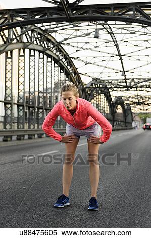 Stock Photography - Young female runner preparing for run on bridge. Fotosearch