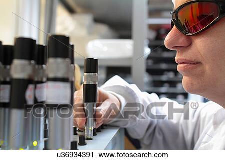 Stock Image - Young female scientist experimenting in laser laboratory. Fotosearch