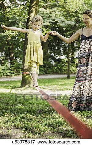 Young girl with mother walking slackline in park View Large Photo Image Stock Photo - Young girl with mother walking slackline in park. Fotosearch