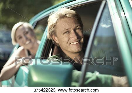 Stock Image - Young male and female leaning out of car window. Fotosearch