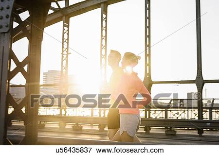 Stock Photo - Young male and female running on bridge. Fotosearch