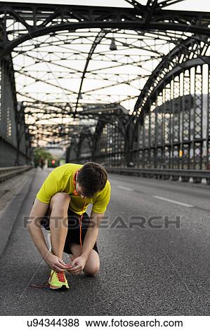 Stock Photo - Young male runner kneeling and tying shoelace on bridge. Fotosearch