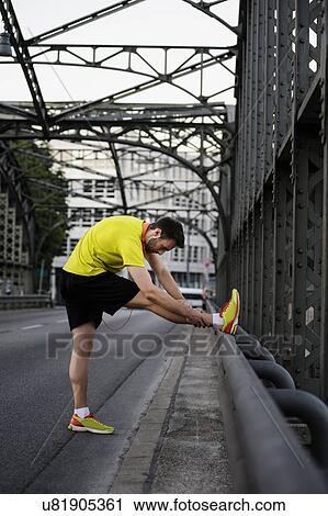 Young male runner stretching legs on bridge View Large Photo Image Stock Image - Young male runner stretching legs on bridge. Fotosearch