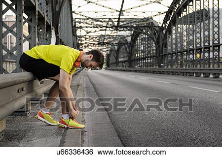 Young male runner tying shoelace on bridge View Large Photo Image Stock Photograph - Young male runner tying shoelace on bridge. Fotosearch
