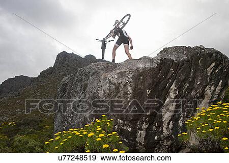 Stock Photo - Young man carrying mountain bike on top of rock formation. Fotosearch