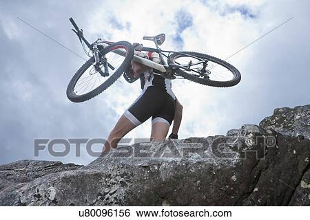 Young man carrying mountain bike on top of rock View Large Photo Image Stock Photograph - Young man carrying mountain bike on top of rock. Fotosearch