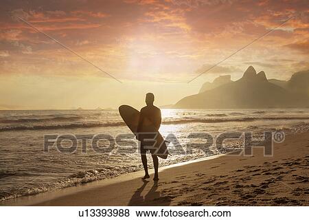 Stock Photo - Young man carrying surfboard on Ipanema beach, Rio De Janeiro, Brazil. Fotosearch