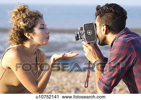 Stock Image - Young man filming woman with vintage camera. Fotosearch