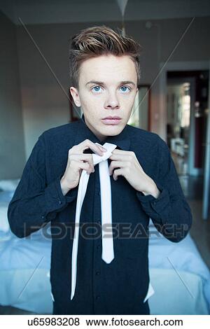 Stock Photo - Young man getting dressed and fastening tie. Fotosearch