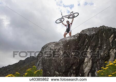 Young man holding up mountain bike on top of rock View Large Photo Image Stock Image - Young man holding up mountain bike on top of rock. Fotosearch